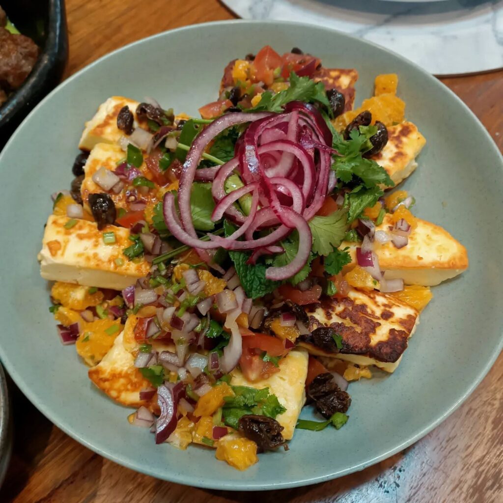 photo of a brightly coloured salad topped with green herbs and red onion rings