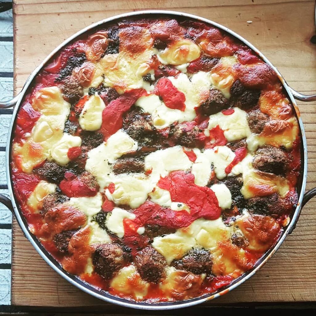 photo of a baked cheesy and tomato meatballs in a round dish on a wooden board background