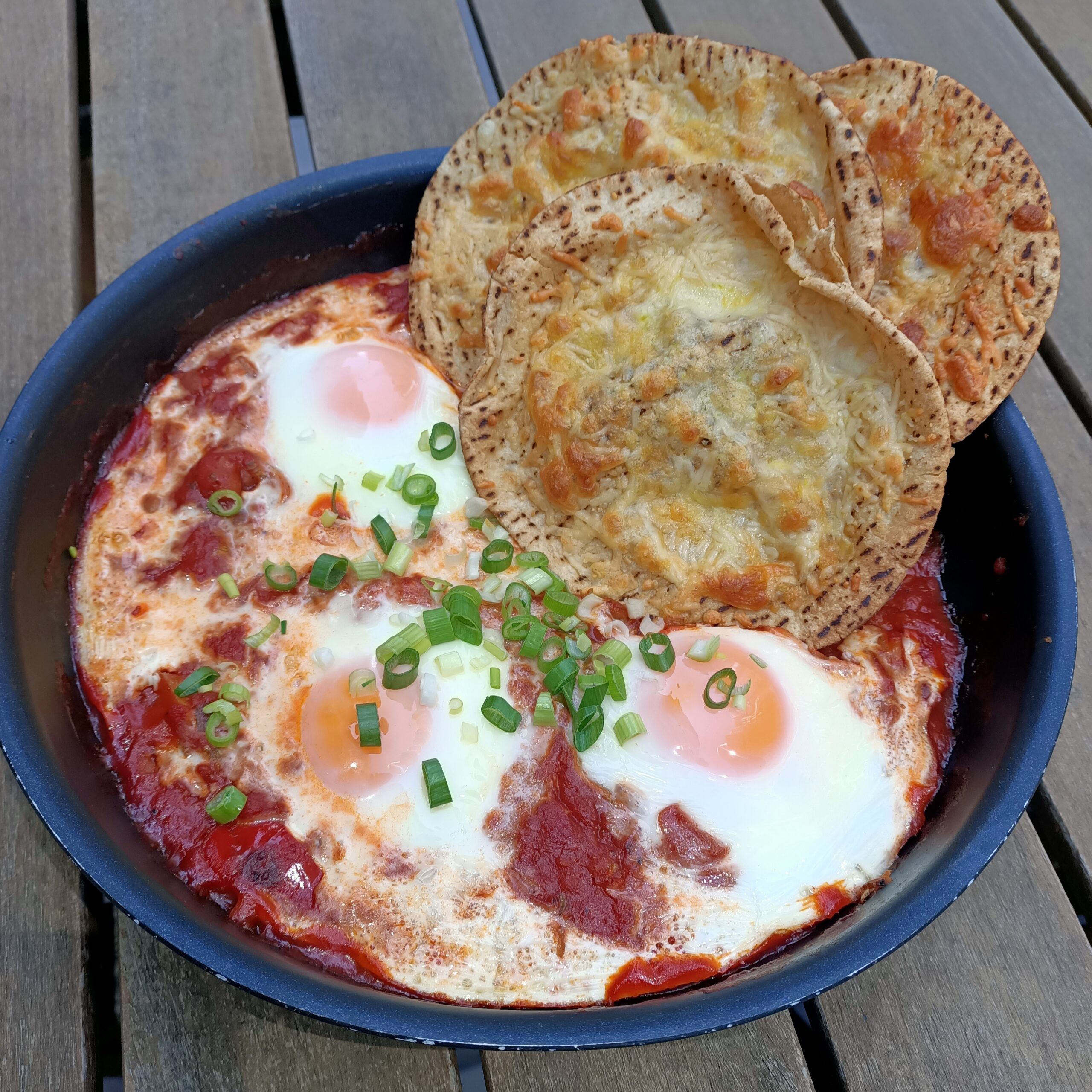 a pan with cooked eggs and tomatoes with cheesy crunchy pita crisps