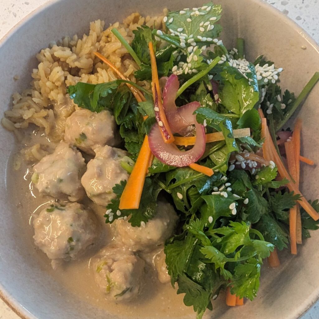 a bowl of beige meatballs and a colourful salad