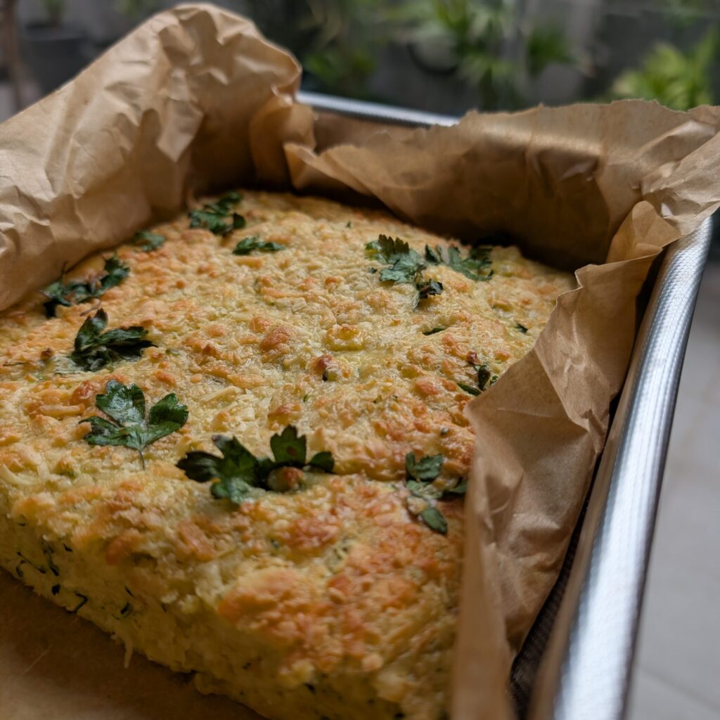 photo of a slice in a silver tin surrounded by brown baking paper a few sprigs of herb on top