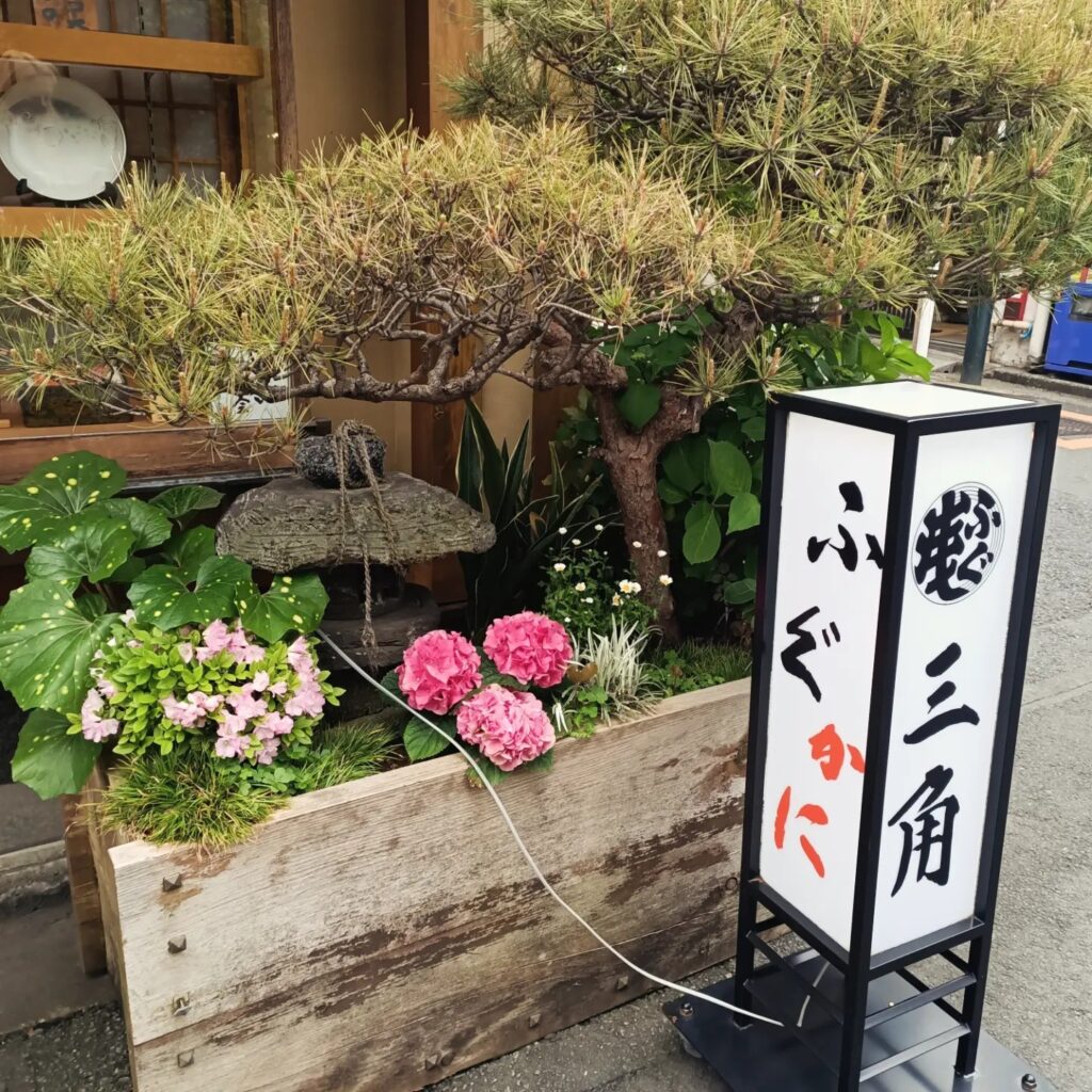 photo of a small garden with plants and flowers with a white and black sign with text in Japanese characters