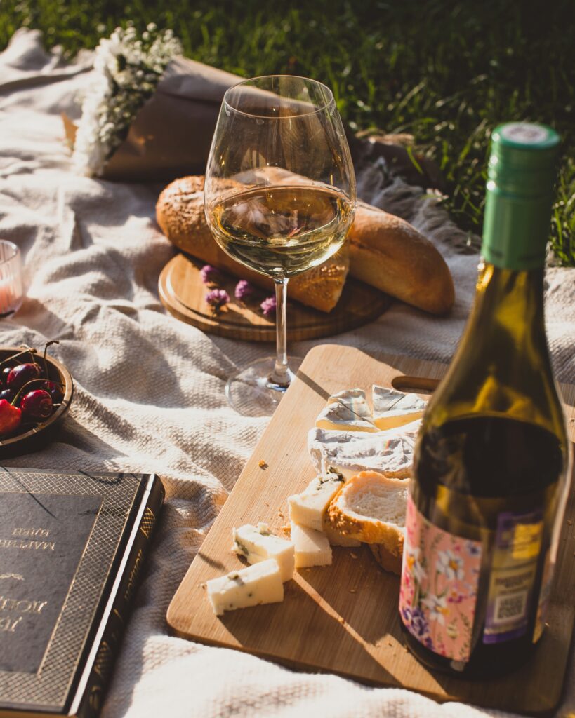 photo of a picnic with wine, cheese and bread on a cloth rug