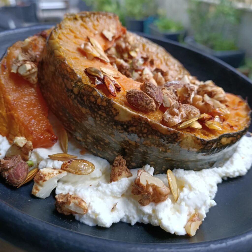 photo of a black plate with some white cheese, wedge of pumpkin and topped with nuts
