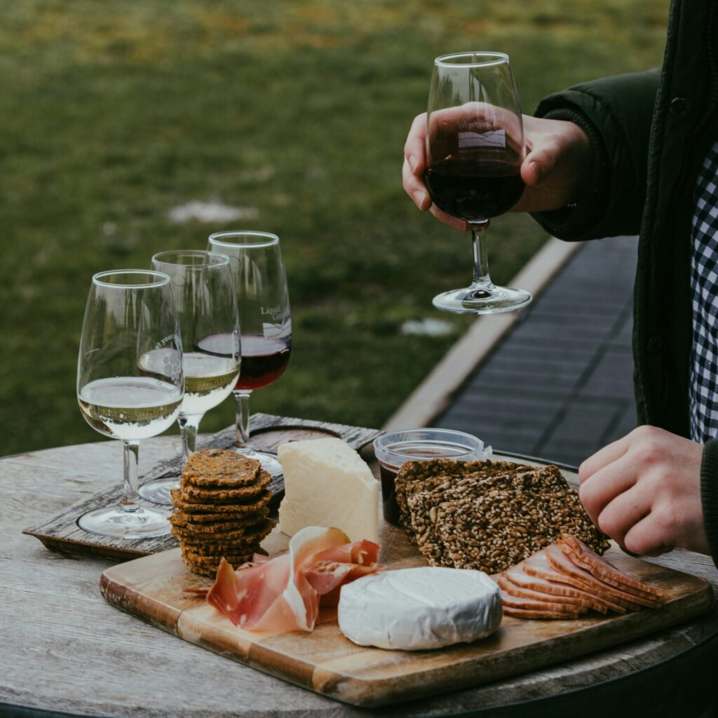 photo of a man standing at a cheeseboard with a red wine in hand