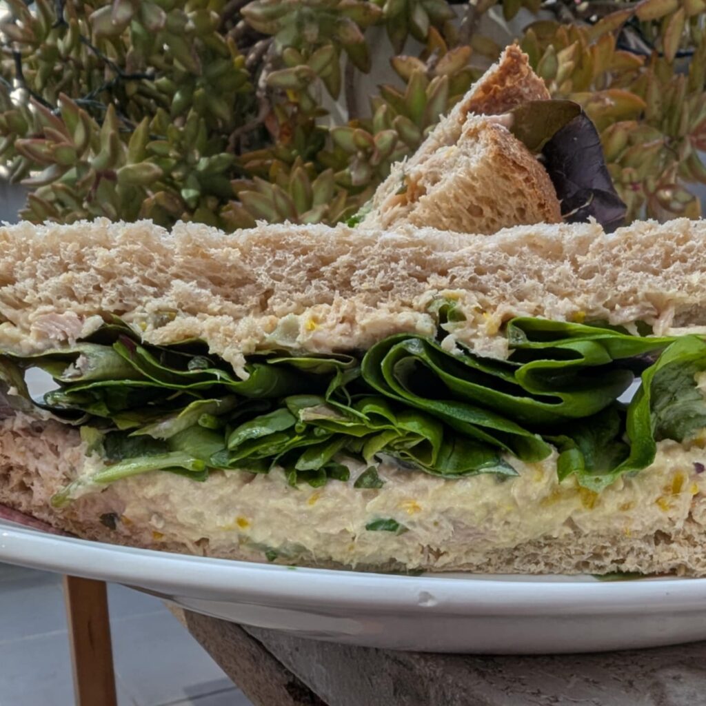photo of a close up of a cut sandwich with lettuce and some beige spread tuna