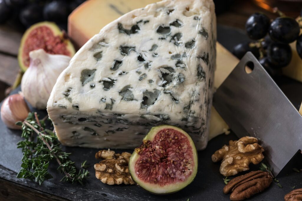 photo of wedge of blue cheese on a wooden board with figs and walnuts