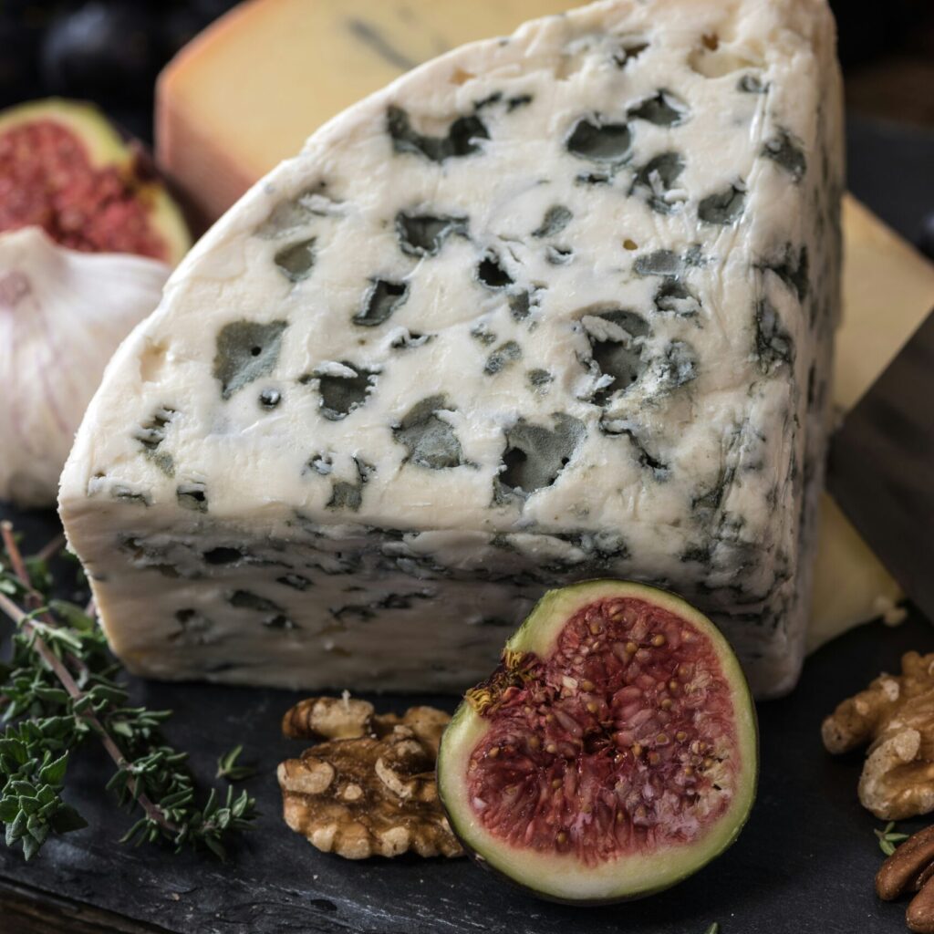 photo of wedge of blue cheese on a wooden board with figs and walnuts