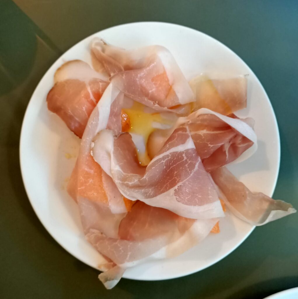 photo of thin slices of proscuitto cured ham and some melon on a white plate