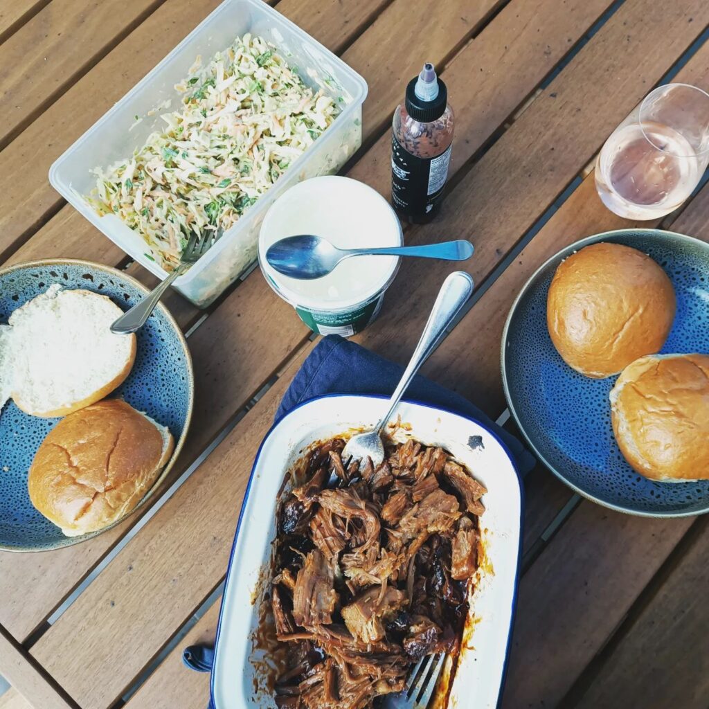 photo of meat in atray, some salad and buns ona wood table