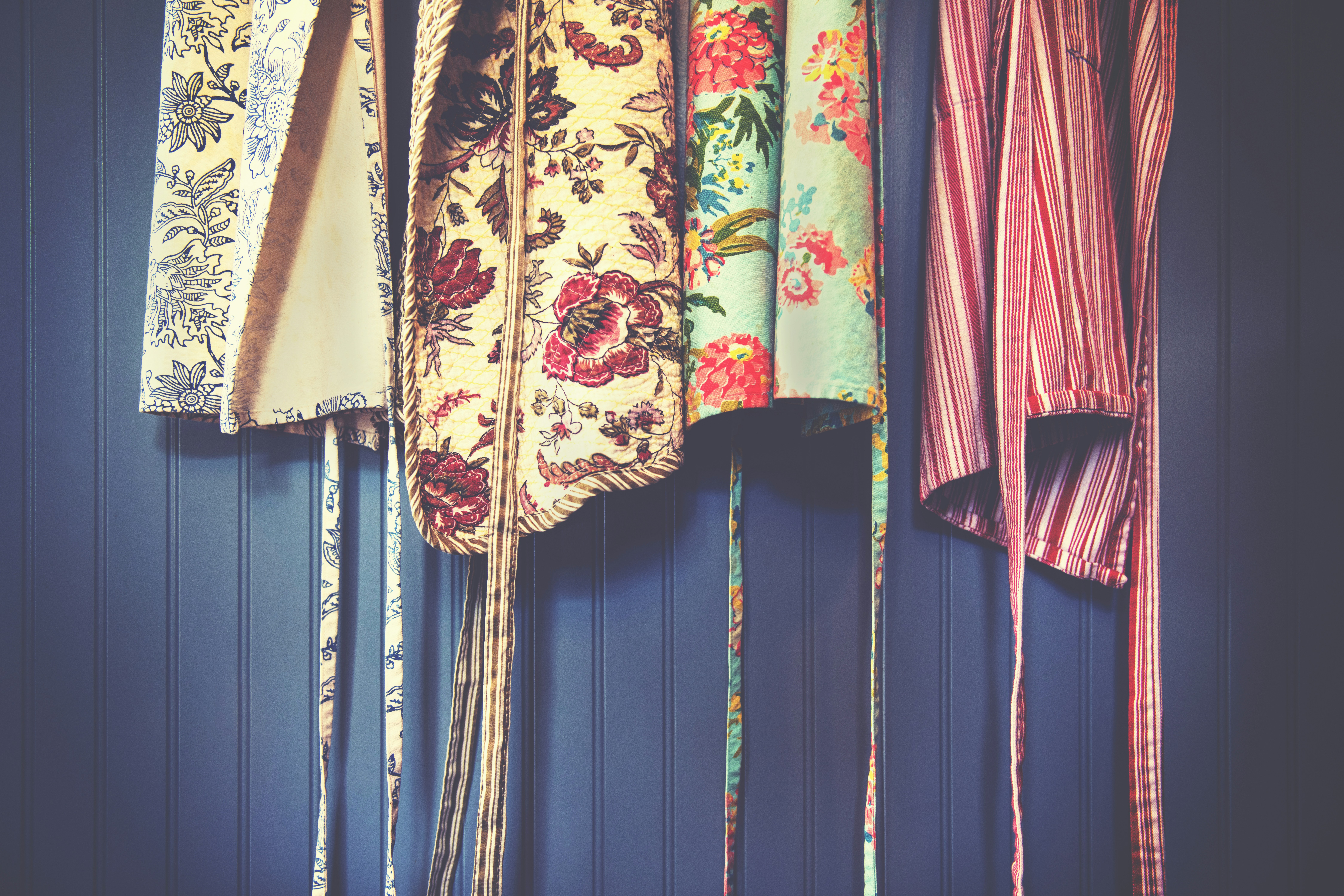 colourful aprons hanging up against a dark blue wall