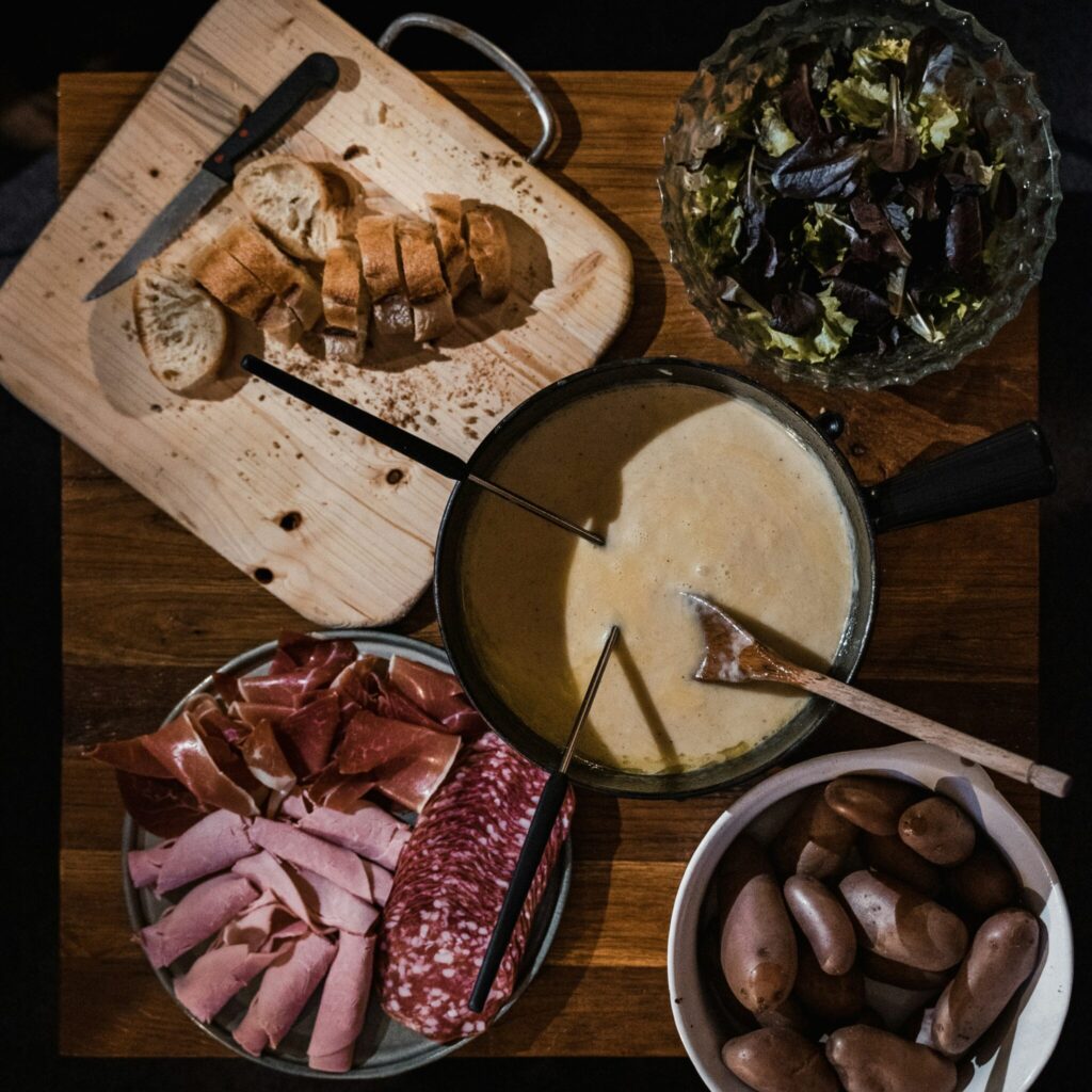 overhead photo of fondue a pot of melted cheese with bread, potatoes and salami