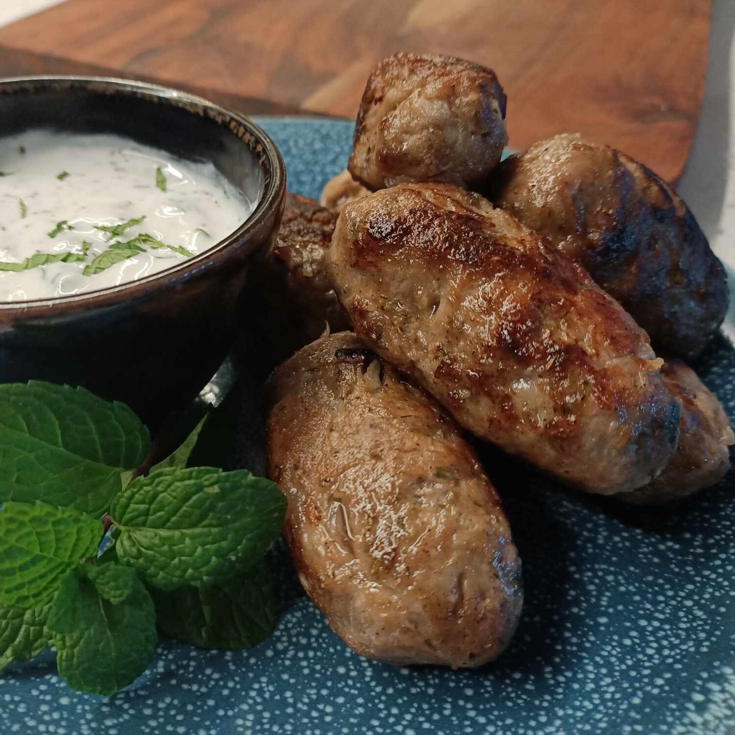 photo of meat oval shaped kofta on a blue plate with white sauce and mint sprigs