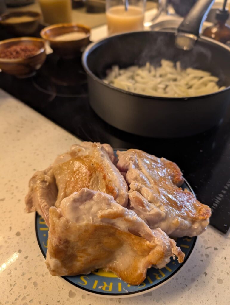 chicken in foreground and a black saucepan with onions frying