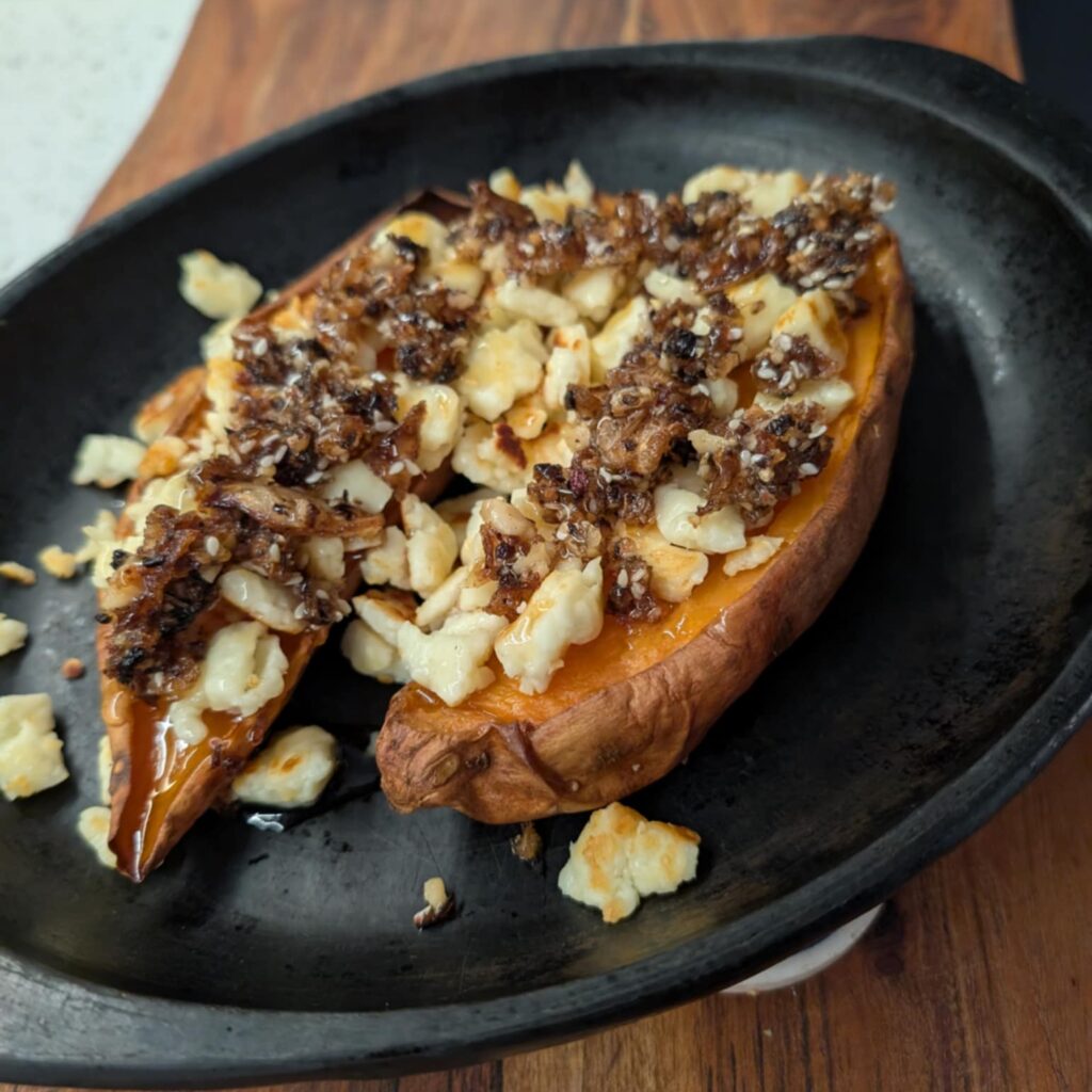 black plate with a sweet potato cut open topped with white and brown crumbles