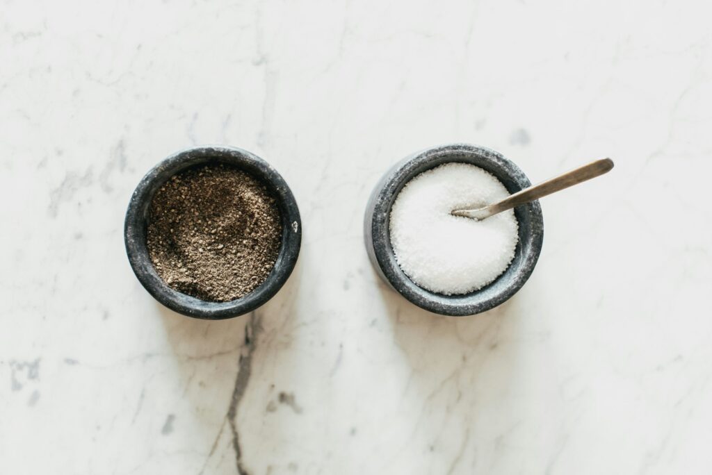 white stone bench with two black bowls with salt crystals and ground black pepper