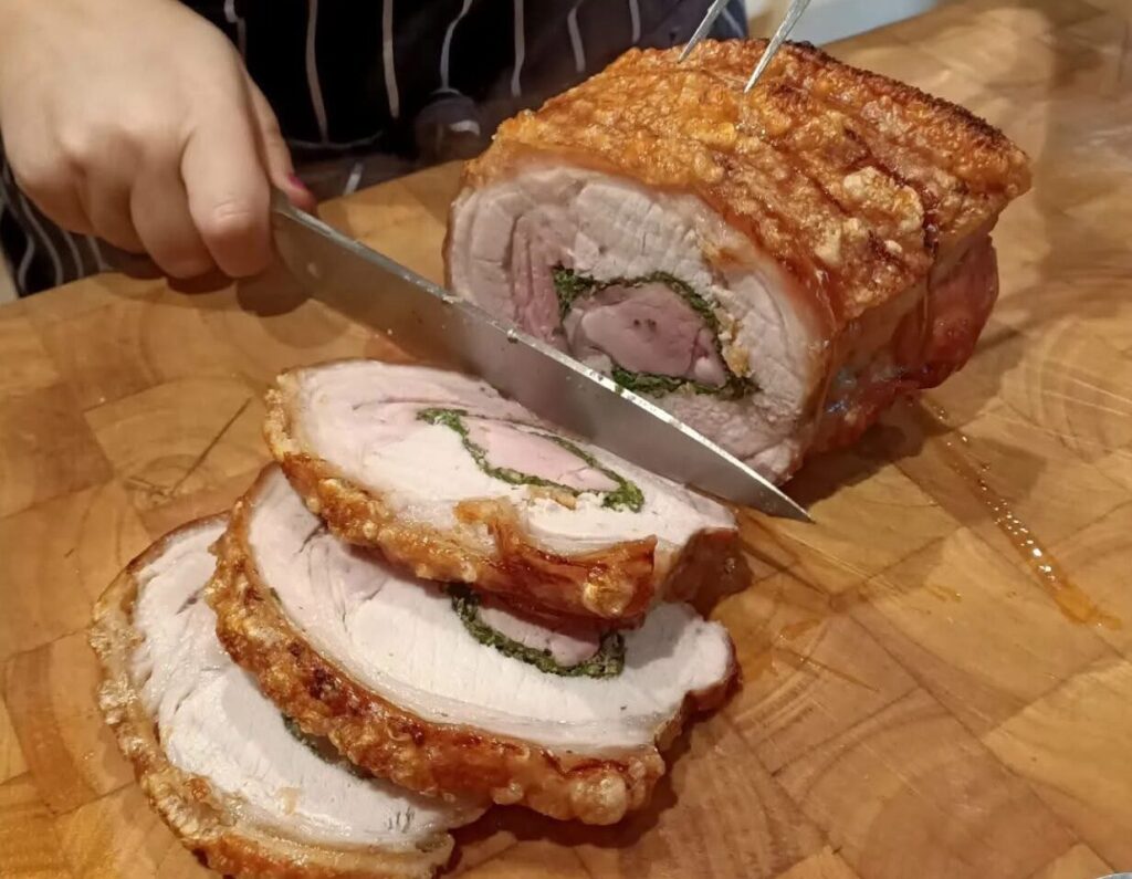 someone slicing up a roast porchetta rolled pork roast