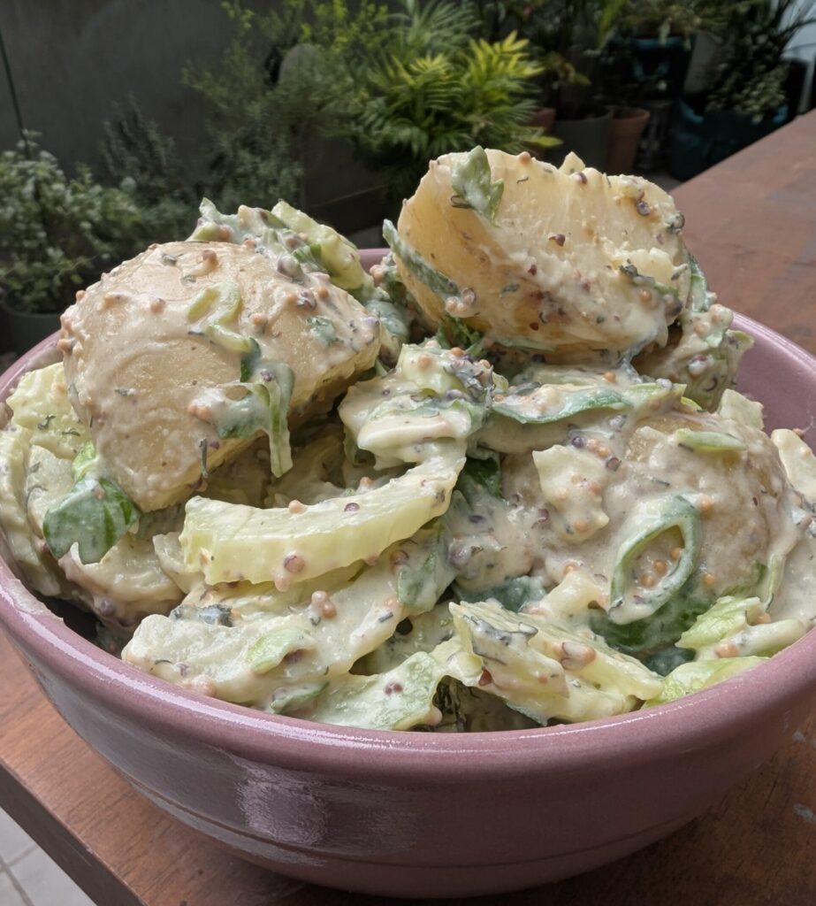 A bowl of potato salad with some plants in the background