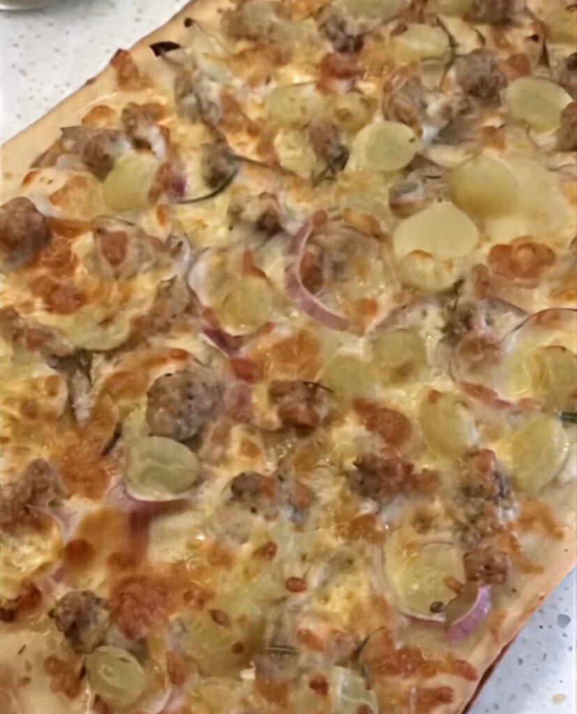 photo of a pizza with bits of meat, grape and sausage and red onion