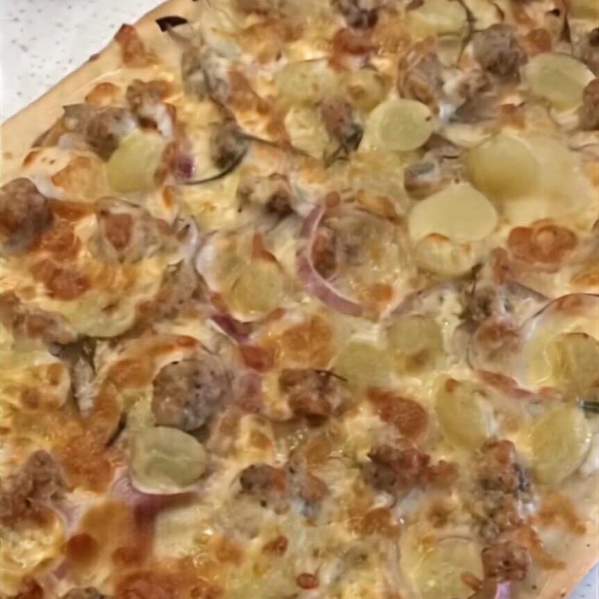 photo of a pizza with bits of meat, grape and sausage and red onion