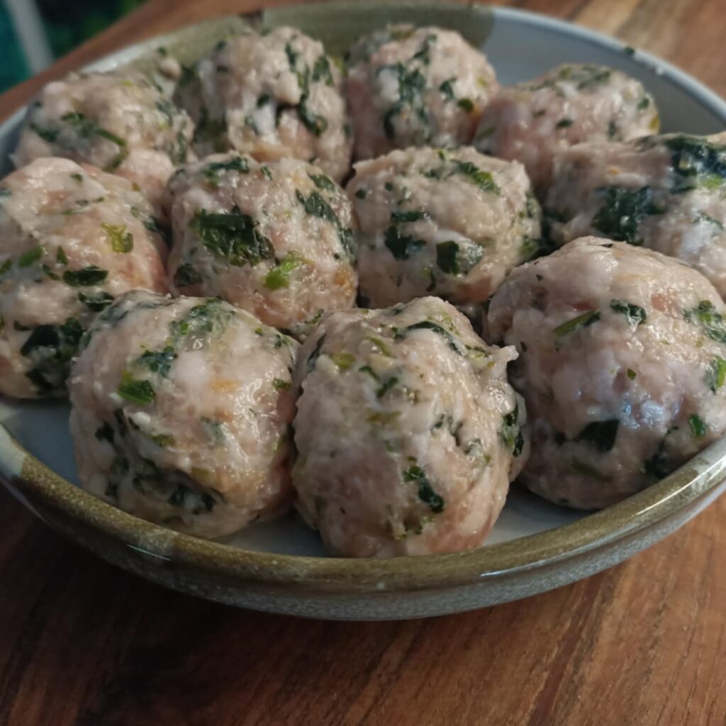 close up photo of raw pork meatballs with flecks of green