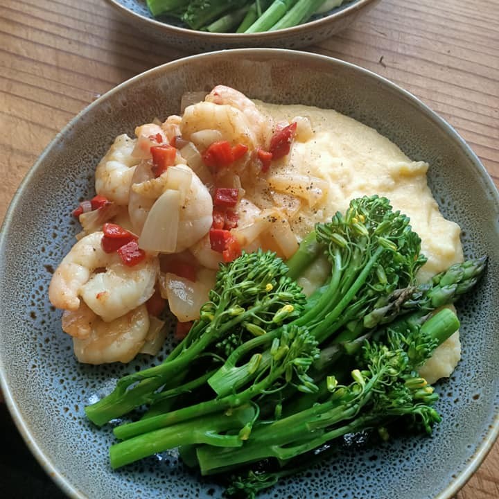 photo of a grey bowl with white creamy cornmeal, green broccolini and cooked prawns