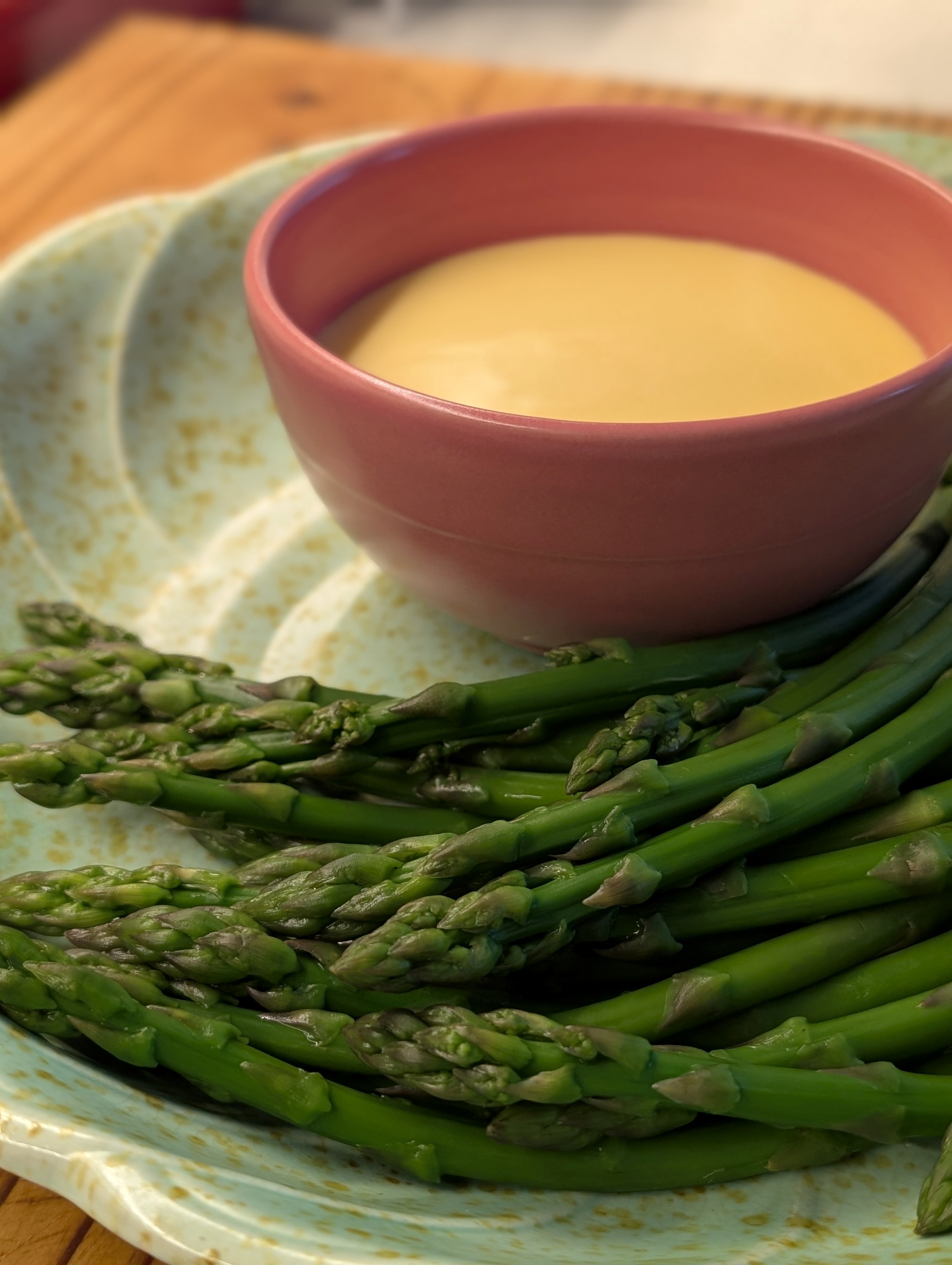 photo of some green asparagus and a yellow sauce in a pink bowl
