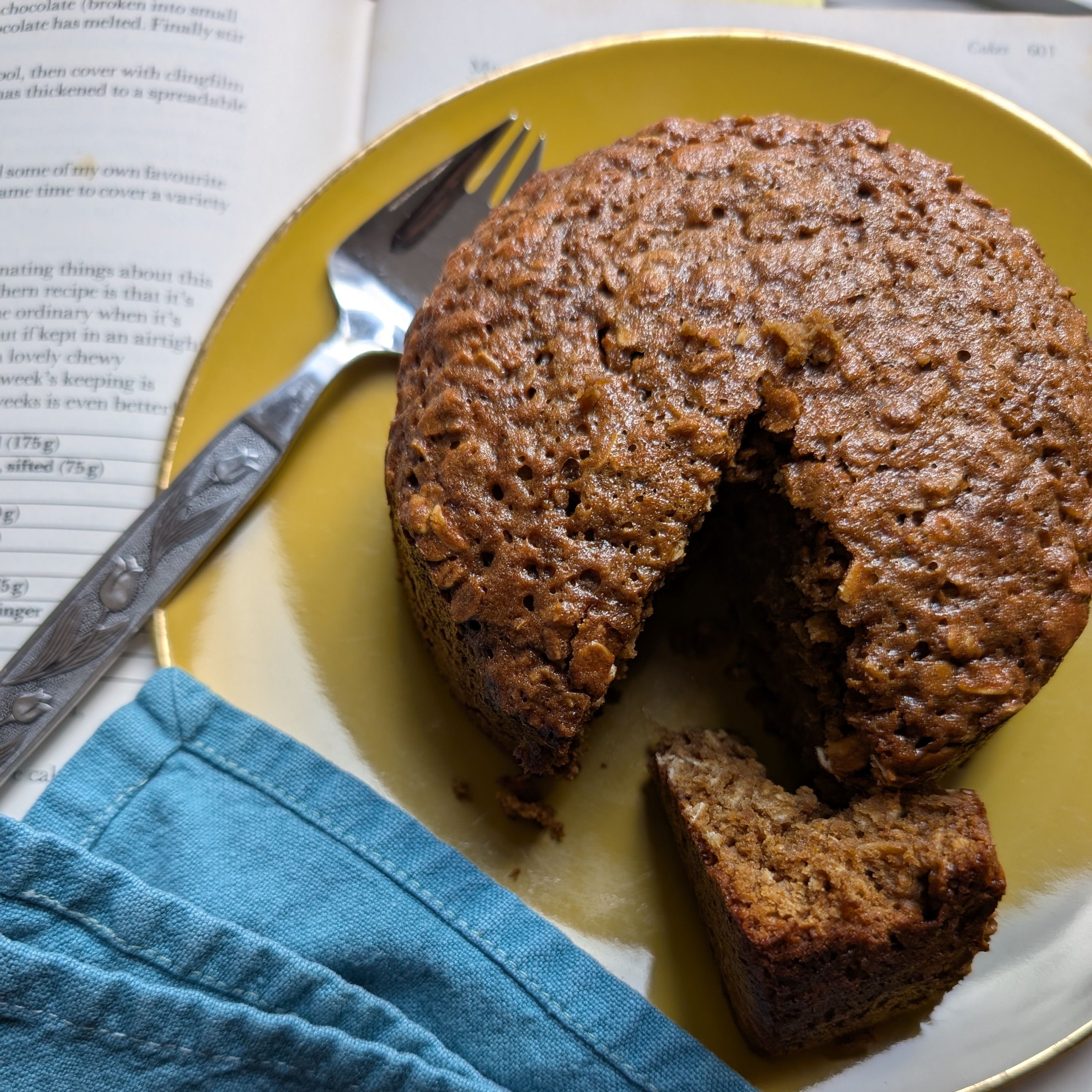 photo of a brown round cake on a yellow plate with a cookbook in the background